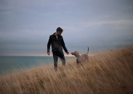 Man with dog walking on grassy landscape against sky