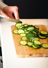 Woman in cutting cucumber on kitchen board.