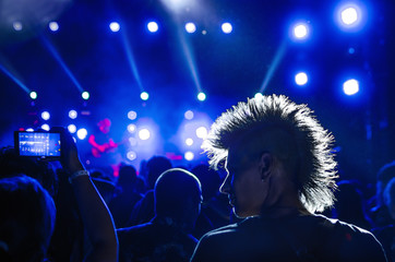 silhouettes of concert crowd and mohawk punk hair style in front of bright stage lights