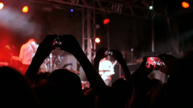 Unrecognizable hands silhouette taking photo or recording video of live music concert with smartphone. Strobing stage lights. Photography, entertainment and technology concept
