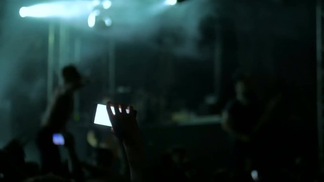 Unrecognizable hands silhouette taking photo or recording video of music concert with smartphone. People partying and jumping in front of the stage. Photography, entertainment and technology concept
