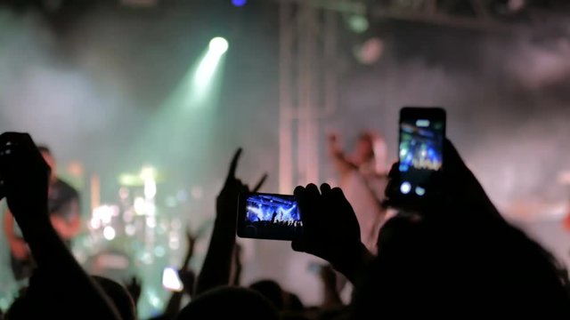 Unrecognizable hands silhouette taking photo or recording video of live music concert with smartphone. Strobing epileptic stage lights. Photography, entertainment and technology concept