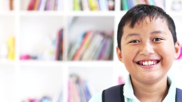 Video footage of a cule male elementary school student looking at the camera while laughing in the library