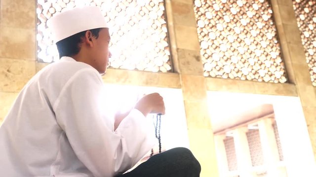 Video footage of a young muslim man sitting in the Istiqlal mosque while praying to the GOD and holding a prayer beads