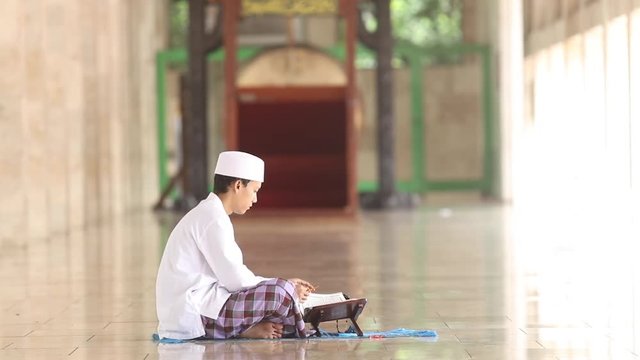 Video footage of a young muslim man reading Quran while sitting in the Istiqlal mosque
