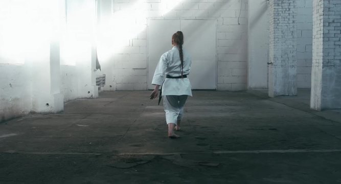 MED Caucasian professional female athlete wearing kimono practicing karate in abandoned warehouse, DX shot. 4K UHD, 60 FPS SLO MO