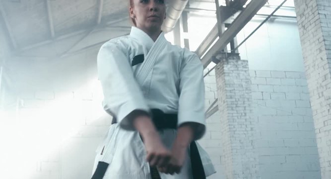 CU Caucasian professional female athlete wearing kimono practicing karate in abandoned warehouse, DX shot. 4K UHD, 60 FPS SLO MO