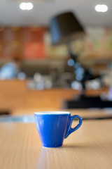 A blue cup of espresso coffee on wooden table in the background of cafeteria