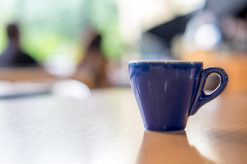 A blue cup of espresso coffee on wooden table in the background of cafeteria