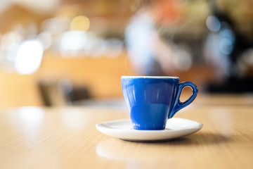 A blue cup of espresso coffee on wooden table in the background of cafeteria