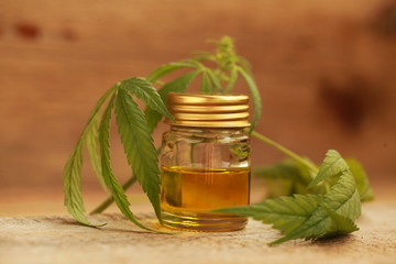 A cannabis leaf and a bottle of hemp oil on a wooden table