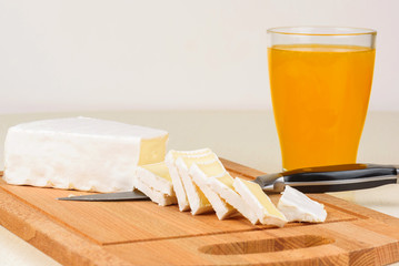 The cheese is sliced on a wooden cutting board and a glass of orange juice for breakfast.
