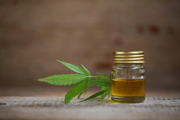 A cannabis leaf and a bottle of hemp oil on a wooden table