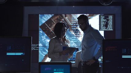 Side view of man and woman communicating in space flight control center. Some elements of this...