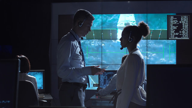 Side view of multiracial man and woman communicating in space flight control center. Elements of this image furnished by NASA.