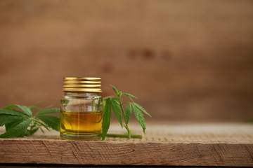 A cannabis leaf and a bottle of hemp oil on a wooden table