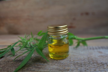 A cannabis leaf and a bottle of hemp oil on a wooden table