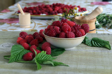 Raspberries in basket on white background with a frame of raspberry leaves, top view.