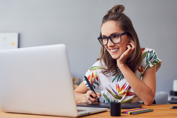 Beautiful smiling young graphic designer sitting at desk in office and working