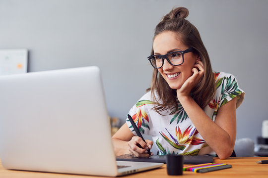 Beautiful smiling young graphic designer sitting at desk in office and working