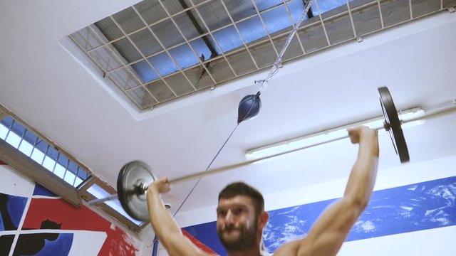 Low angle view of muscular male athlete lifting heavy barbell weight inside boxing ring.