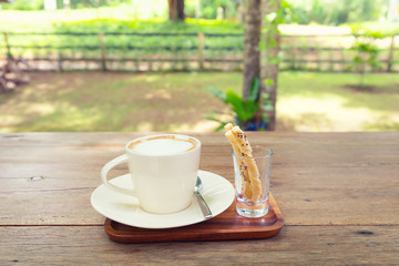 Coffee cup and pastry on wooden table with nature background.