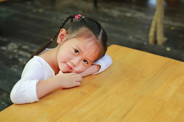 Portrait cute little girl lying on the empty wood table looking straight at camera. Back to School concept.
