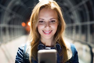 Woman in the city at night holding smartphone, texting.