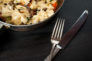 vintage silver cutlery along with a pan of fresh cooked pasta on dark backgrond, horizontal image