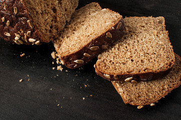 close up of a delicious fresh baked slices of bread with sunflower seeds on a dark table, horizontal image