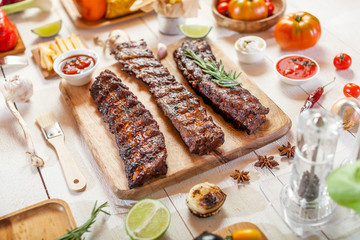 Spicy hot grilled spare ribs from a summer BBQ served with chips, corn and fresh tomatoes on an old wooden cutting board