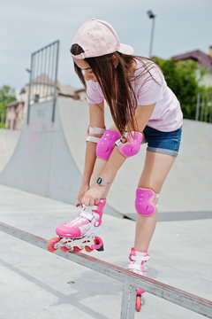 Portrait of a beautiful girl wearing cap, t-shirt and shorts putting on rollerblades outdoor next to the lake.
