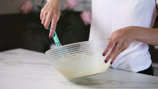 Closeup view of woman's hands mixing ingredients to prepare dough in the the bowl using whisk. Home cooking. Slowmotion shot