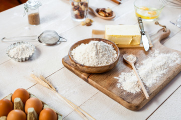 Baking ingredients in rural kitchen - dough recipe ingredients (eggs, flour, milk, butter, sugar) and rolling pin on wooden white table.