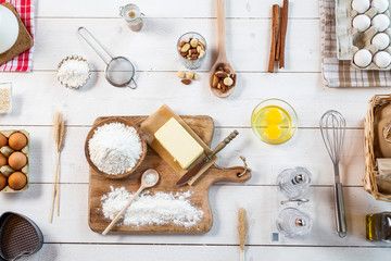 Baking ingredients in rural kitchen - dough recipe ingredients (eggs, flour, milk, butter, sugar) and rolling pin on wooden white table. Top View