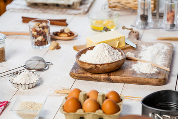 Fototapeta na wymiar Baking ingredients in rural kitchen - dough recipe ingredients (eggs, flour, milk, butter, sugar) and rolling pin on wooden white table.
