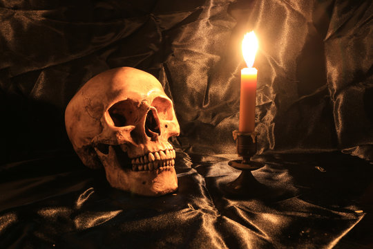Still Life of skull  with fetters and candle on black fabric with texture with candle light in dim light night. image tone from candle light in night time.