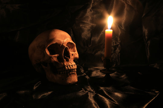 Still Life of skull  with fetters and candle on black fabric with texture with candle light in dim light night. image tone from candle light in night time.