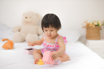 Little cute asian baby girl sitting on bed playing