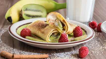 Homemade pancake with vanilla curd, raspberries, kiwi and banana pieces sprinkled with cocoa
