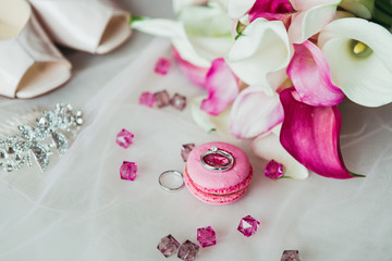 Obraz na płótnie Canvas Wedding rings on the pink macaron with pink gems, shoes and flowers