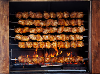 Roasted chickens on spit grilled over fire of a big barbecue