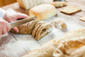 Male hands cutting fresh bread on the wooden table, selective focus