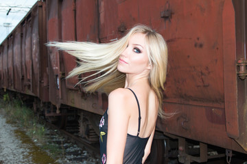 Fototapeta premium Beautiful blonde girl walking on rail tracks, romantic look, from back, wind tin the hair