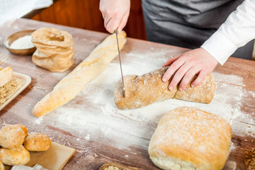 Male hands cutting fresh bread on the wooden table, selective focus