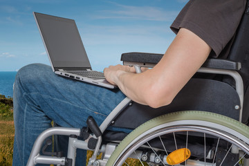 Obraz premium Handicapped disabled man on wheelchair is working with laptop outside.