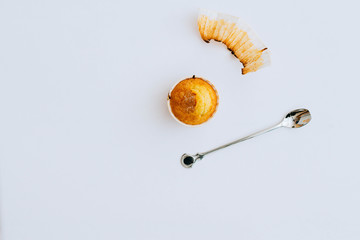 One orange cupcake on a white background, a cake wrapper, a metal spoon, minimalism