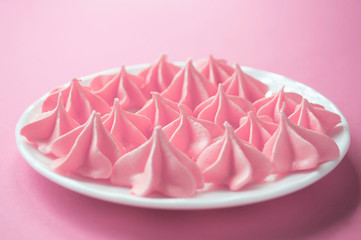 Meringues in the white plate on the pink background. Selective focus.