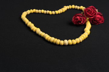 Ancient yellow trade beads in necklace with red roses on black cloth background