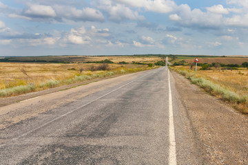 Old road in the Ukrainian steppe in summer under blue sky with clouds